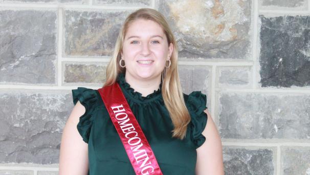 Olivia stands smiling in front of a Hokie Stone wall wearing a maroon Homecoming Court sash