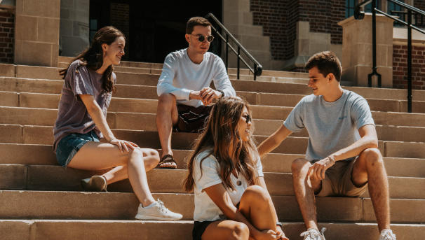 Four students sit on the steps of Pomerene Hall, talking with one another