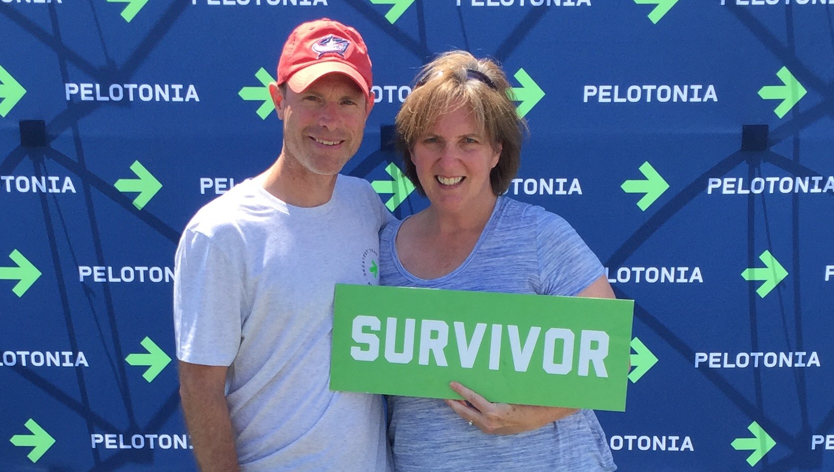 A man has his arm around a woman. She holds a green sign with 'Survivor' printed on it