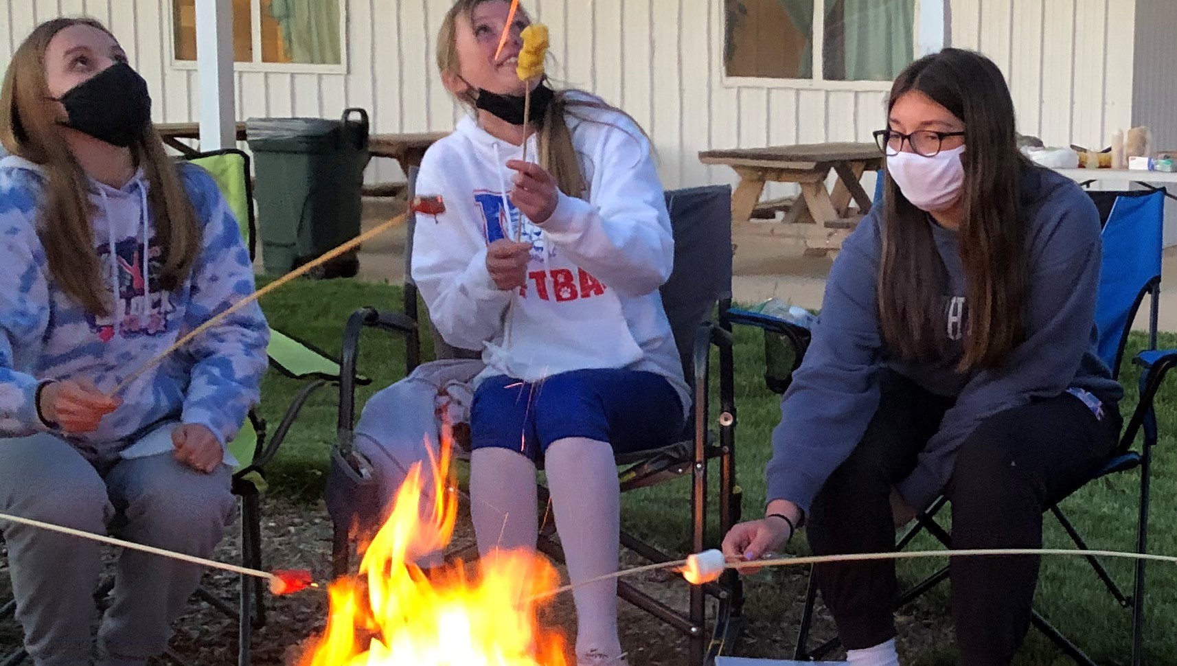 Three individuals sitting around a campfire roasting marshmallows, sitting in lawn chairs