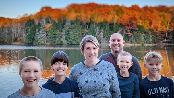 Six individuals standing in front of a lake during the fall. Two adults and four children