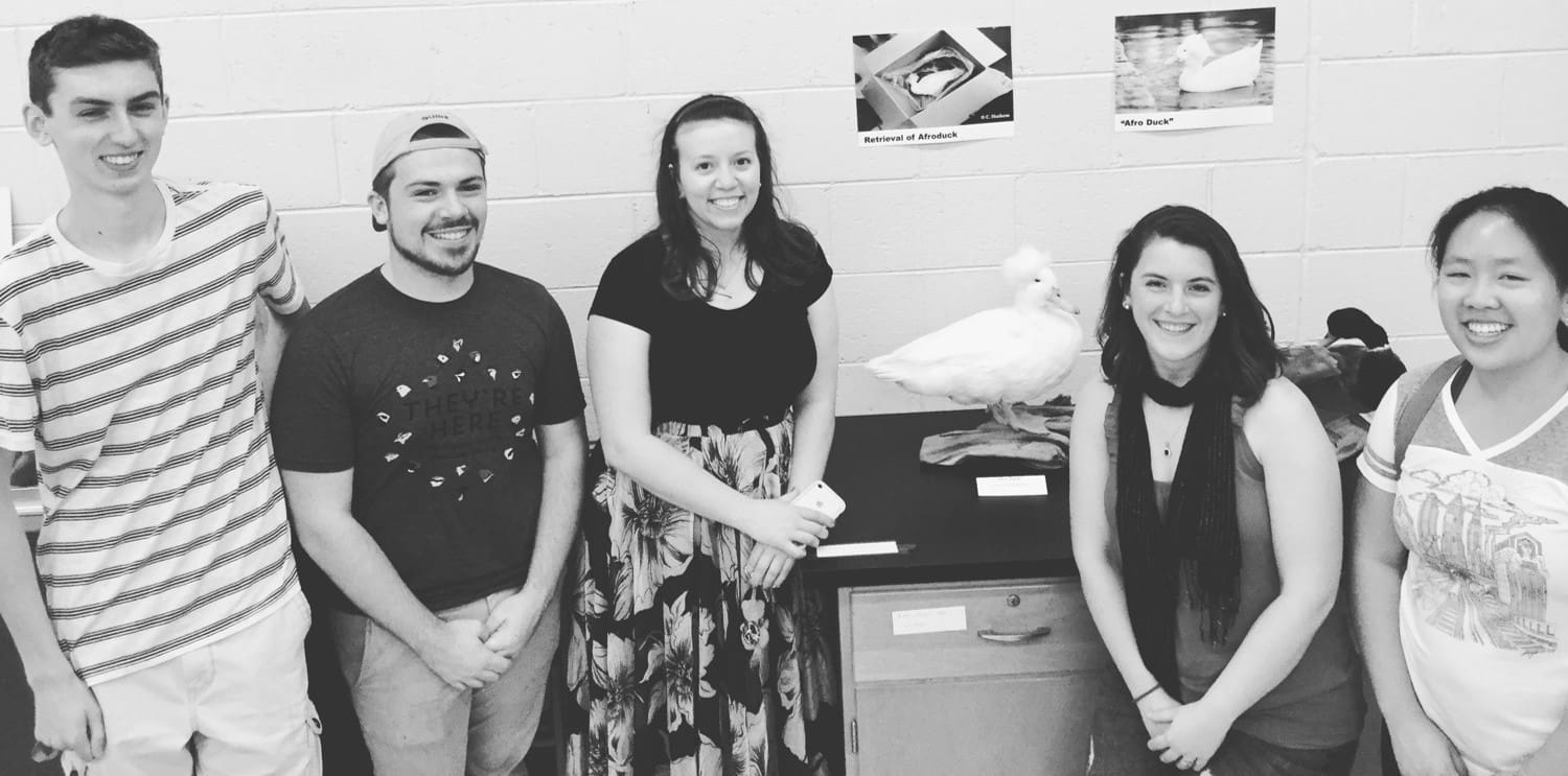 Five students next to a taxidermied bird