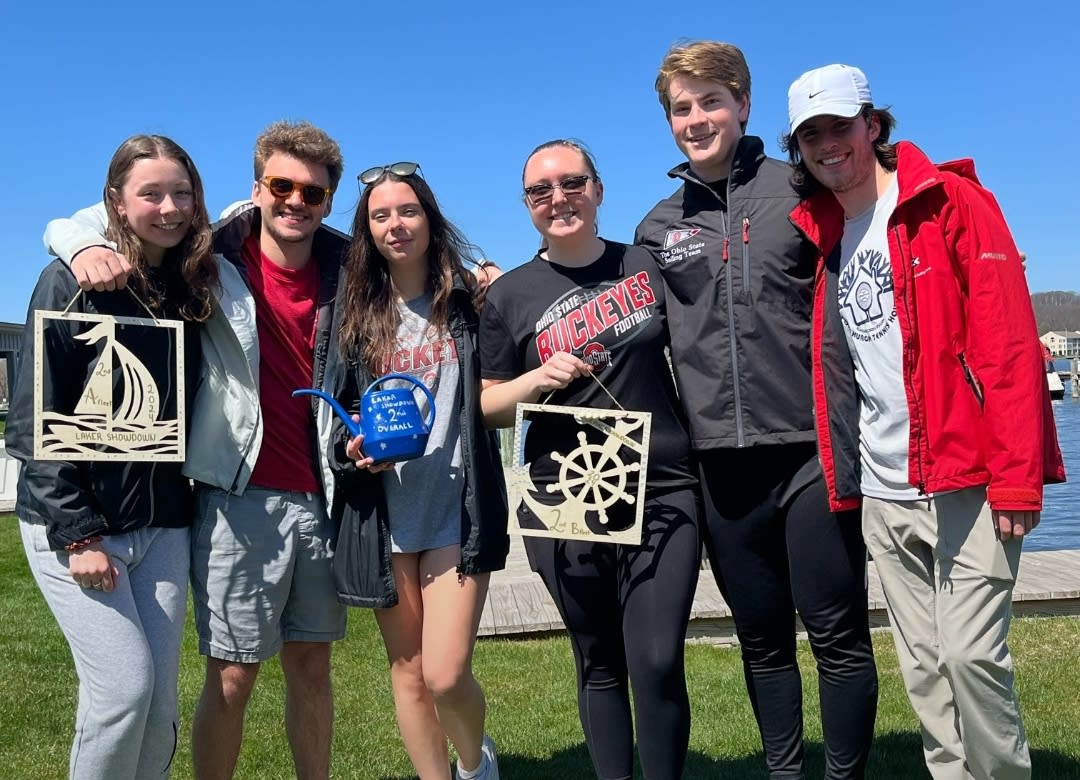 Six people smiling outside, holding sea awards