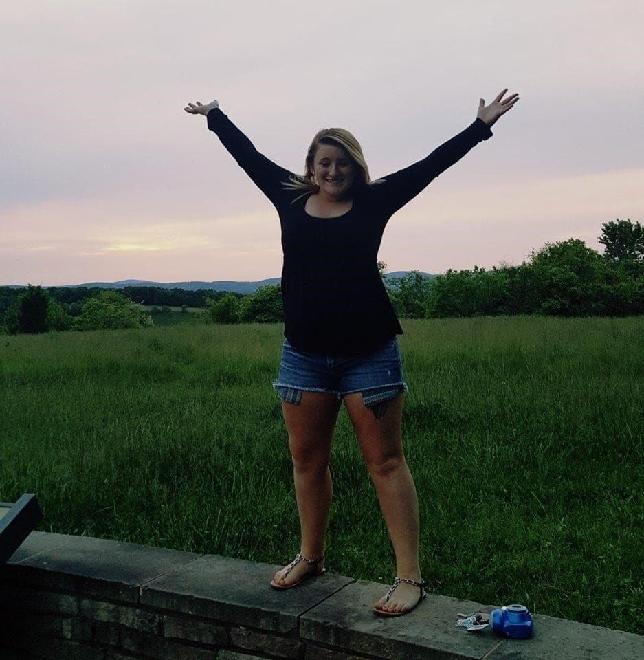 A girl stands on a brick fence, arms outstretched