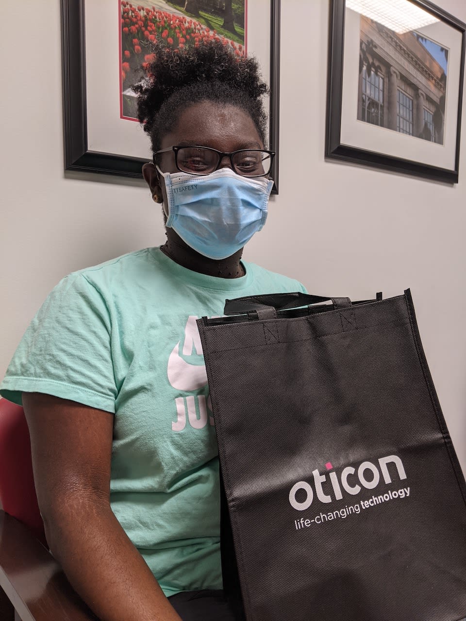 A masked girl sitting, holding a Oticon tote bag