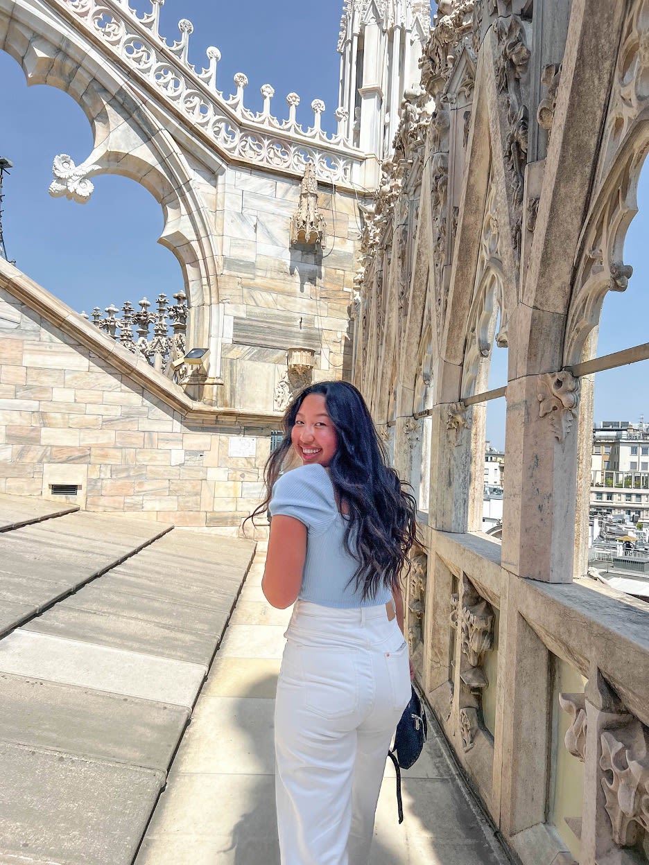 A woman smiles on a stone walkway with arches