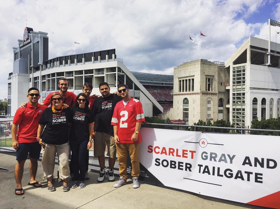 7 individuals stand at Sober Tailgate sign