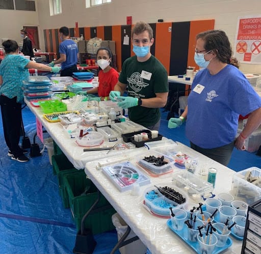 Three volunteers stand by a table full of supplies
