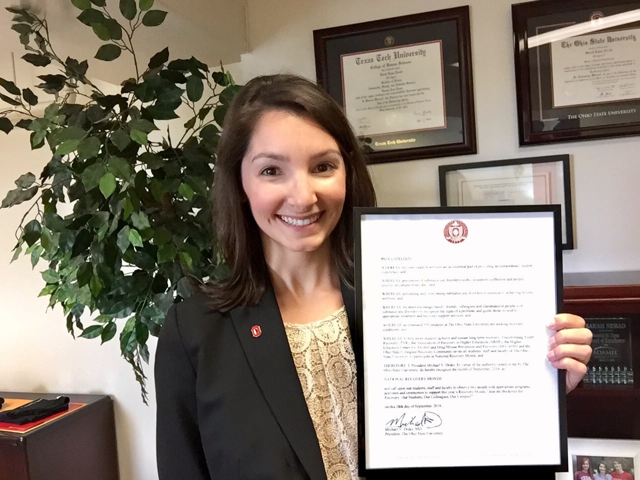 A woman holds a framed document, smiling