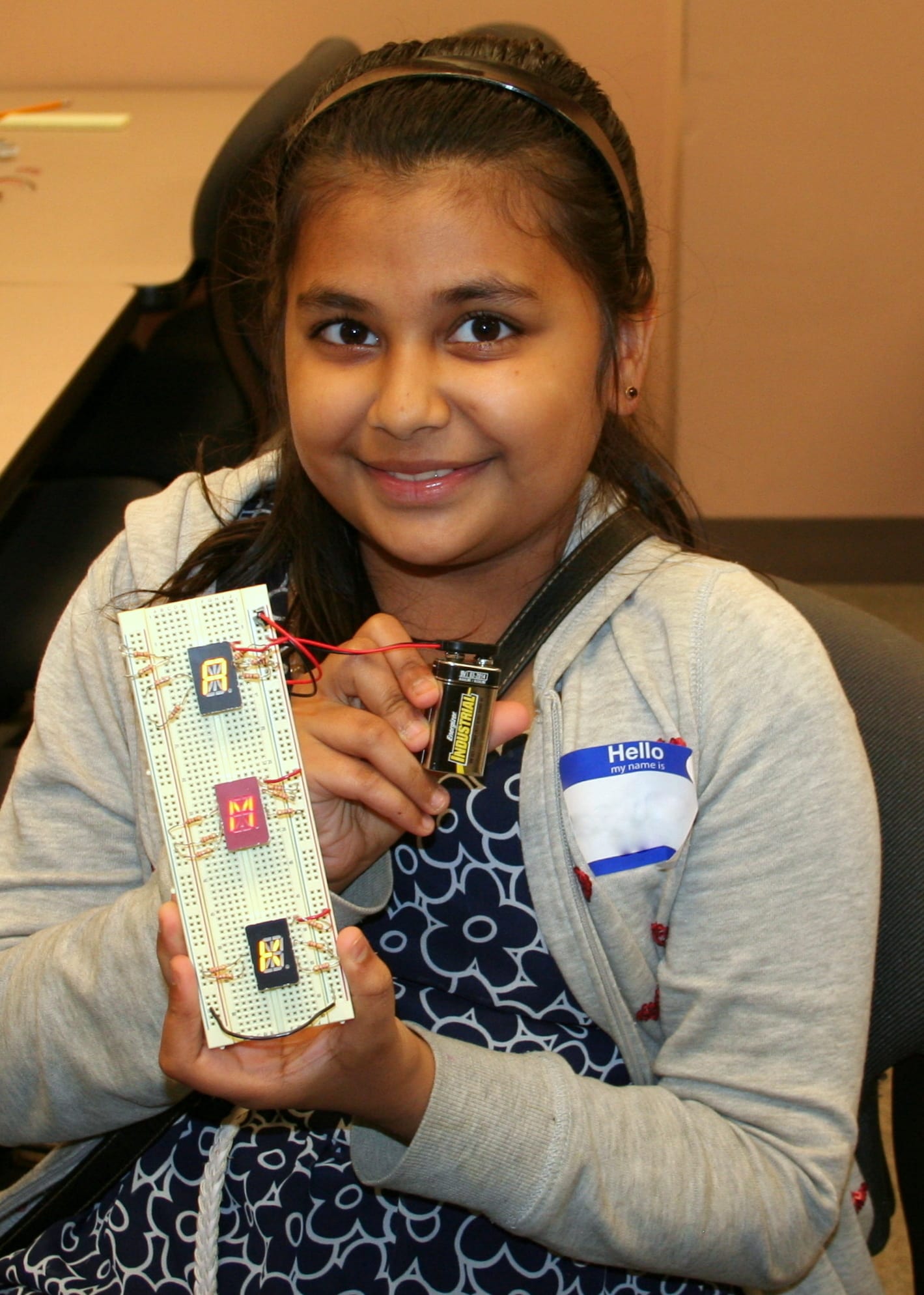 A circuit board reads AMK; a girl holds it