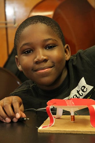 A boy smiles from behind his creation