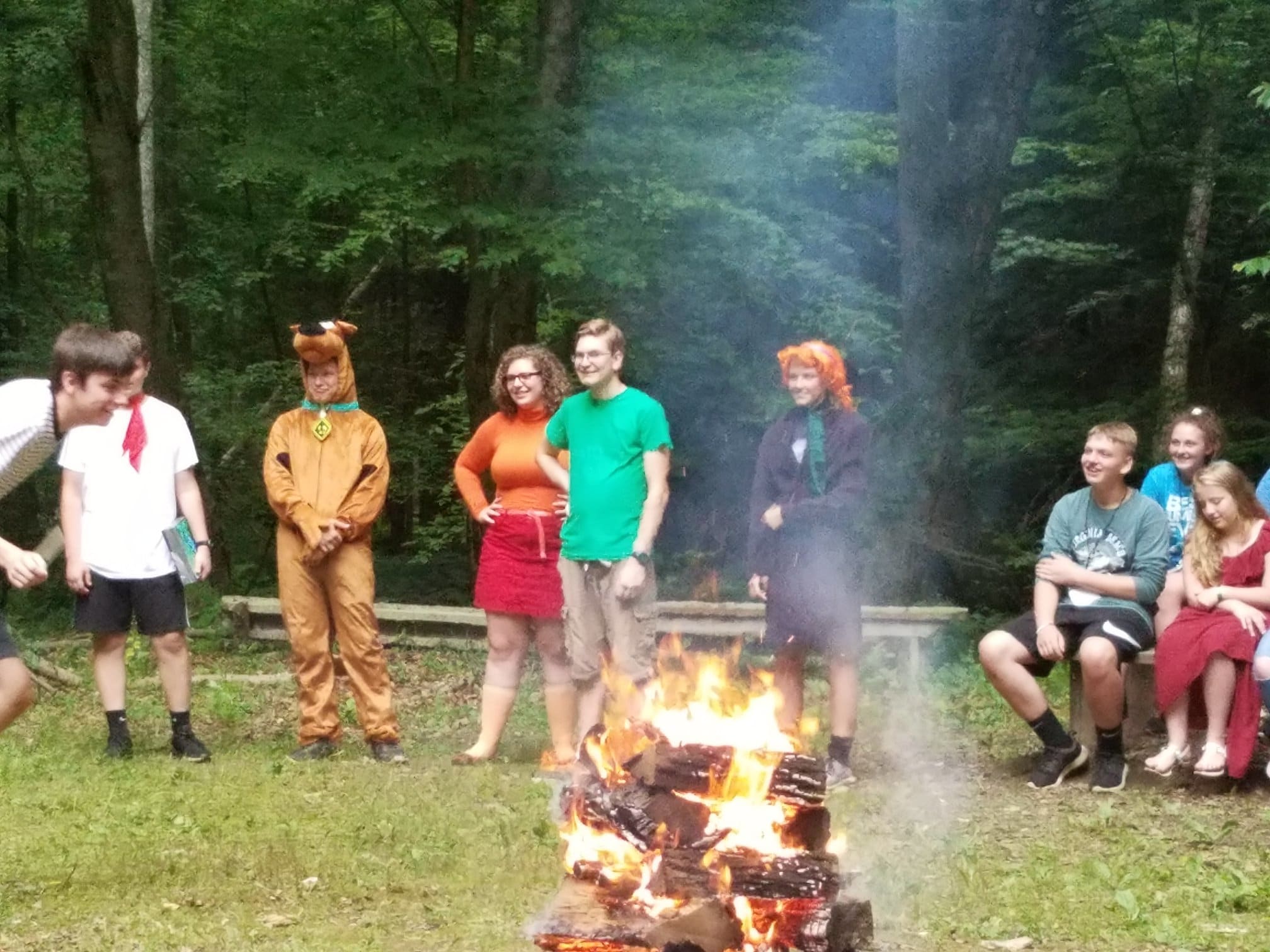 Dressed up campers gathering around a lit campfire