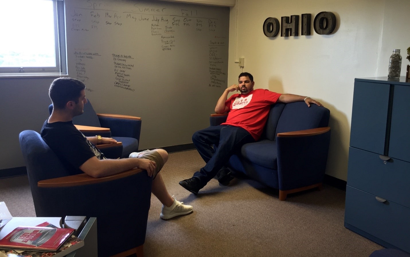 Two students talking, one on couch, other on chair