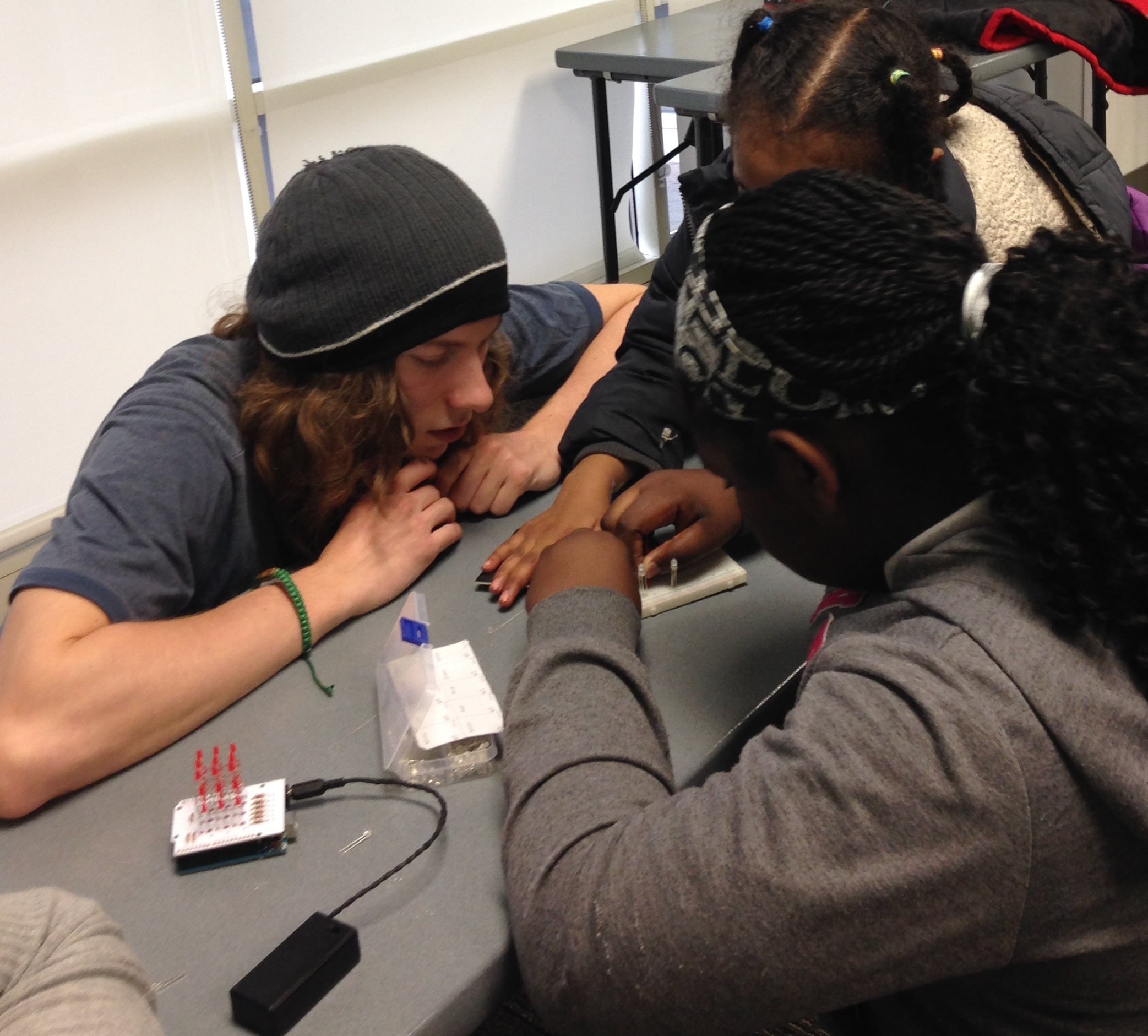 Three students congregate around a wire board