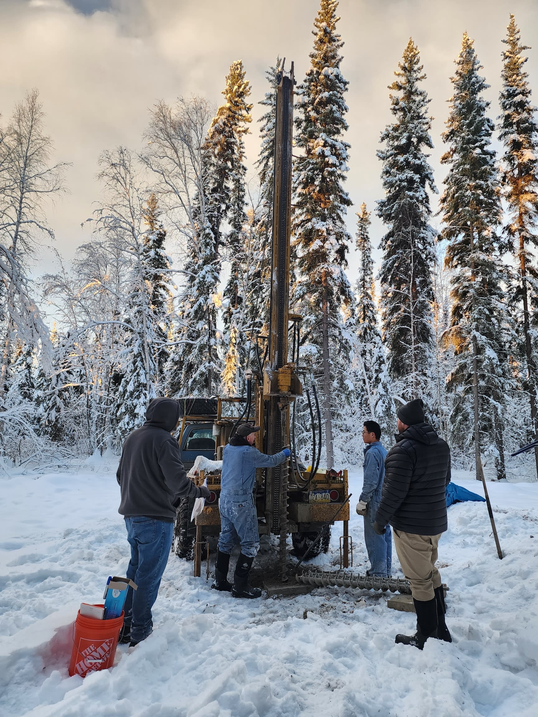 Four people by a large drill in the forest.