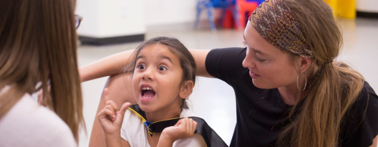 small child talking to a teacher with a student teacher helping