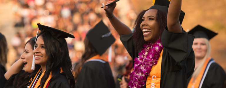 3 students smiling and clapping at graduation ceremony