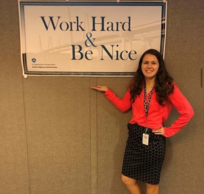 Brittney Welch posed with her hand beneath a 'Work Hard & Be Nice' hanging poster. 