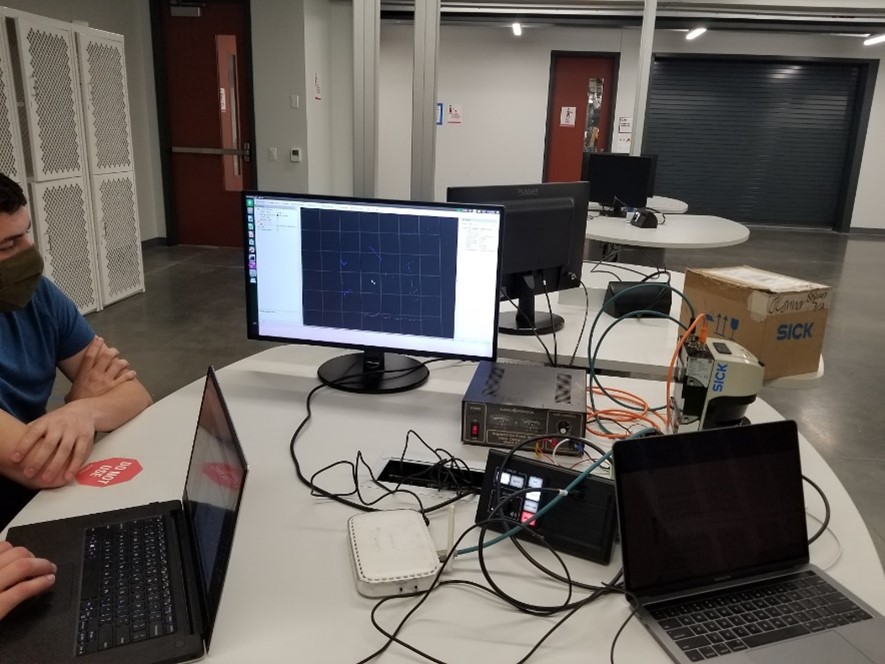 A table with two laptops, a monitor, and wiring connected to a LiDAR computer vision system.