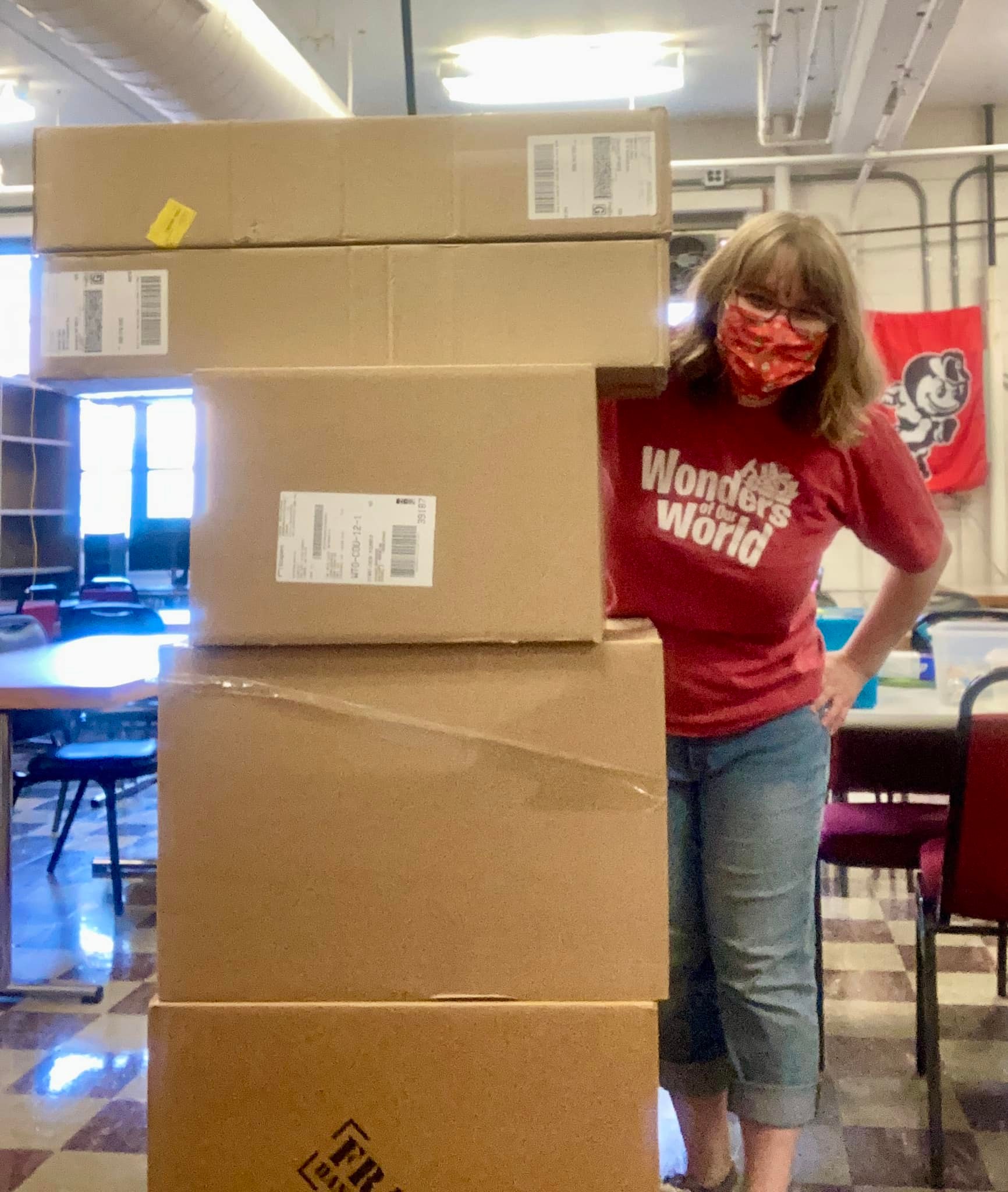A woman wearing a mask standing next to a tall pile of filled cardboard boxes