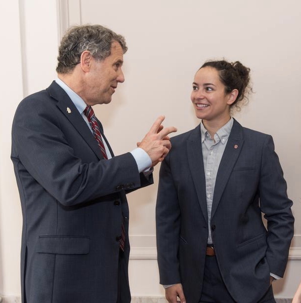 Katy Scruppi speaking with Sherrod Brown against a white wall 
