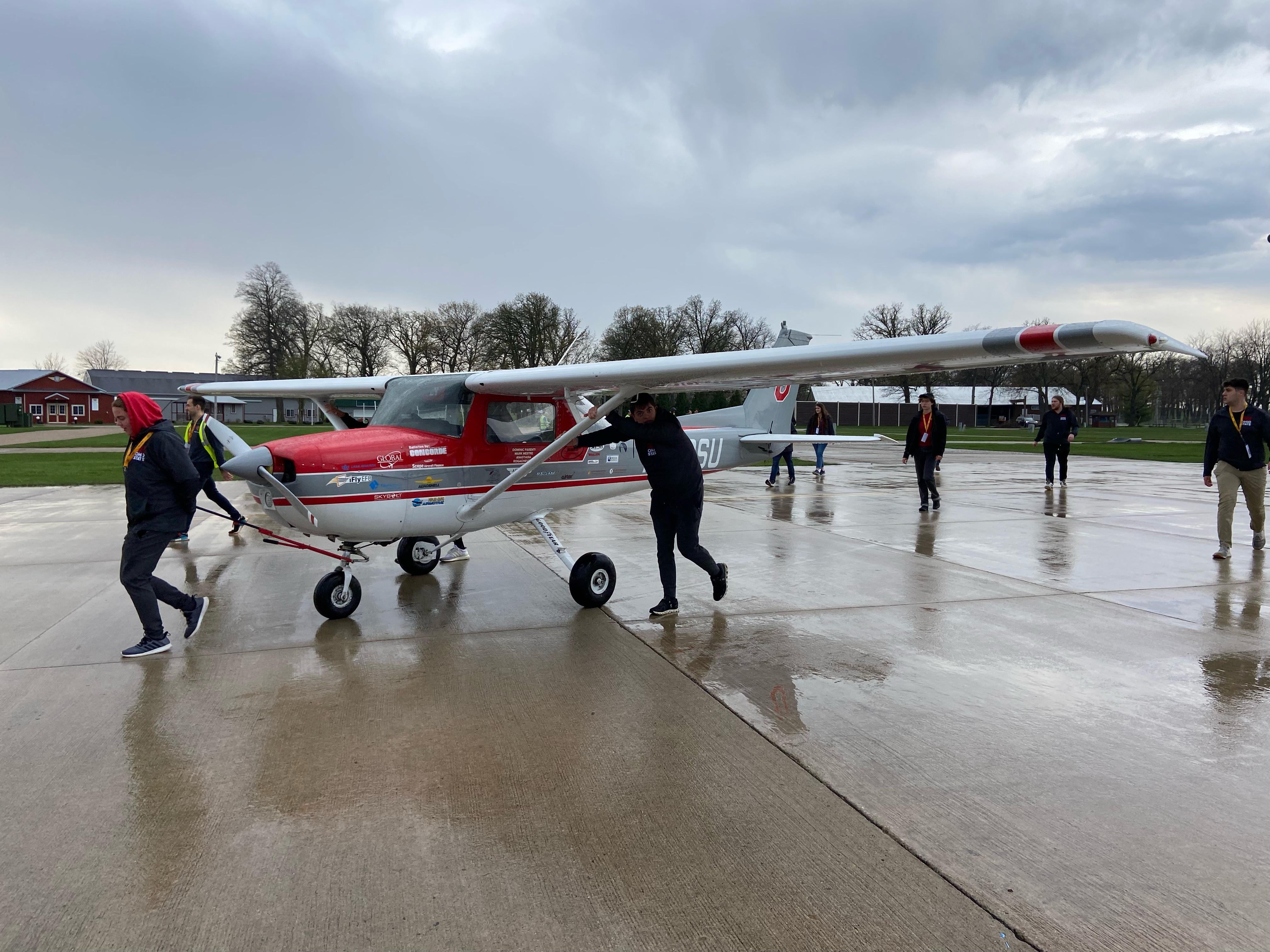 The Ohio State plane being pushed on a wet runway by two team members