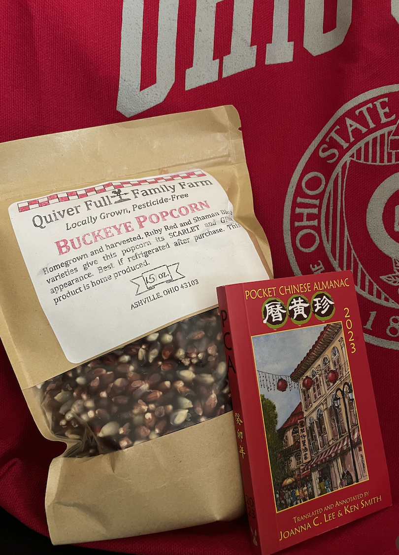 A collection of items including Buckeye Popcorm, a Pocket Chinese Almanac book, and an Ohio State blanket