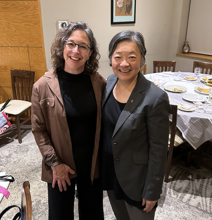 Alice and Pam posed together for a picture. In the background, a table is set with plates and food 