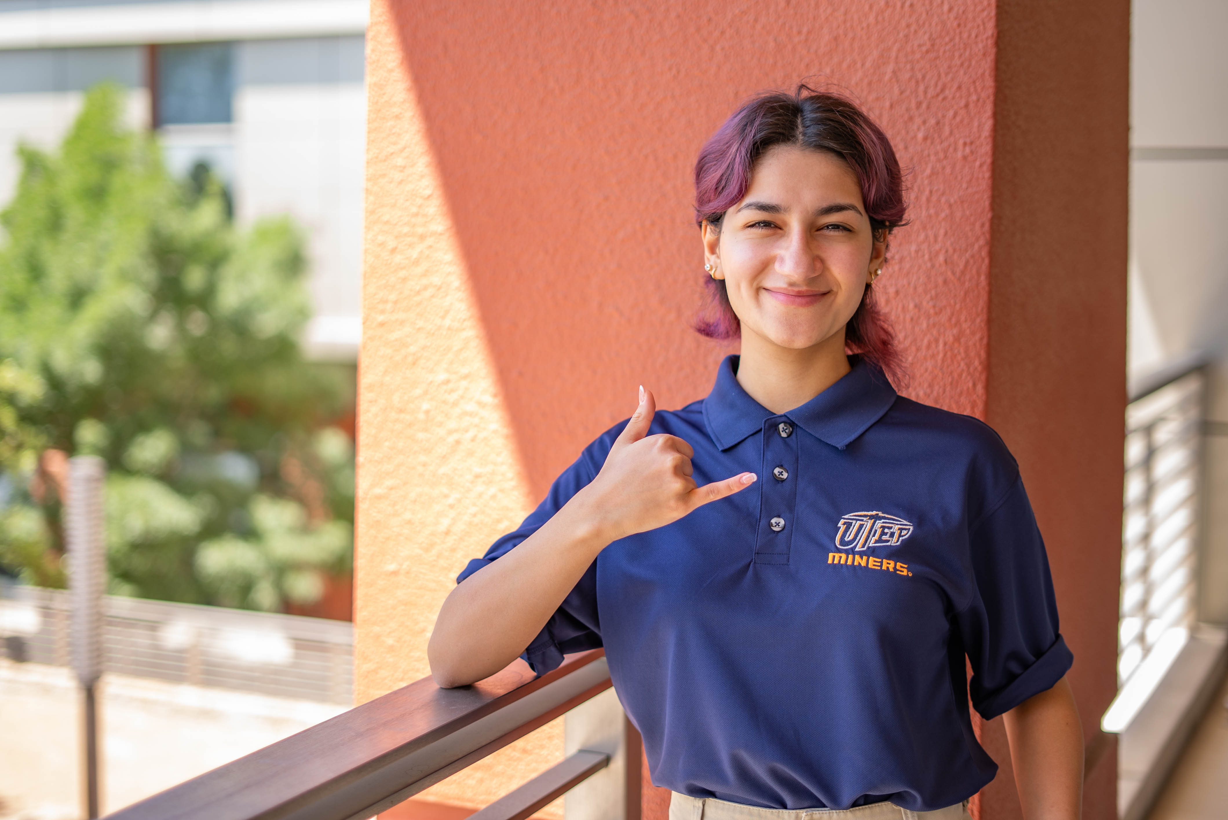 UTEP student, Alyssa, wearing navy blue UTEP polo shirt, posed with pick up on a bridge