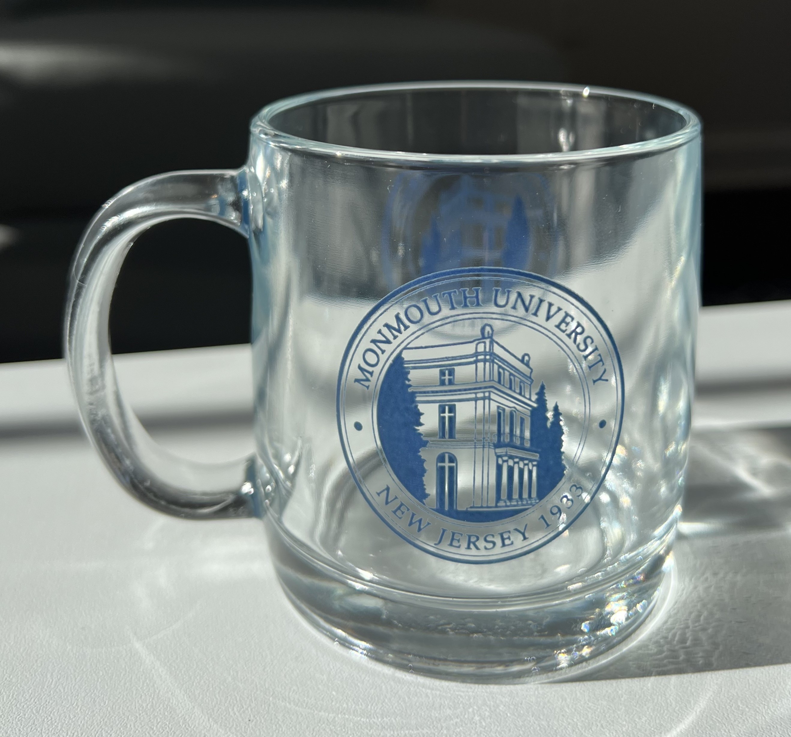 clear glass mug with a navy blue monmouth university seal on both sides of the mug