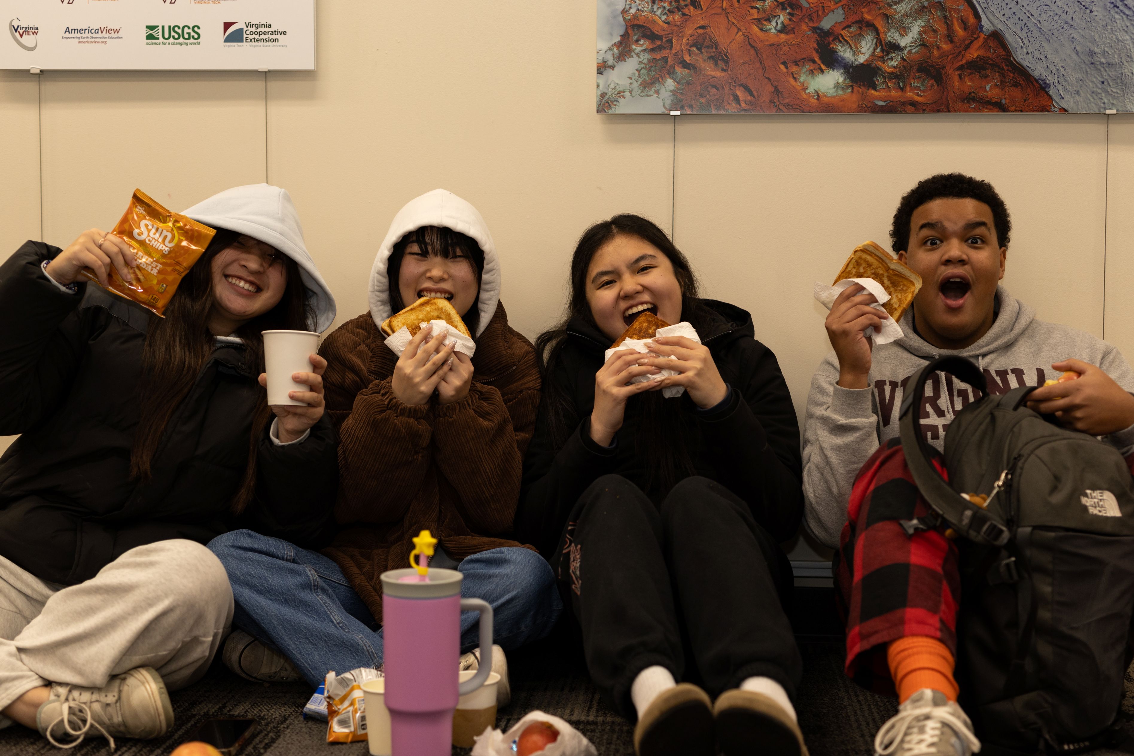 Students smile while they eat their sandwiches and show off their snacks for the camera.
