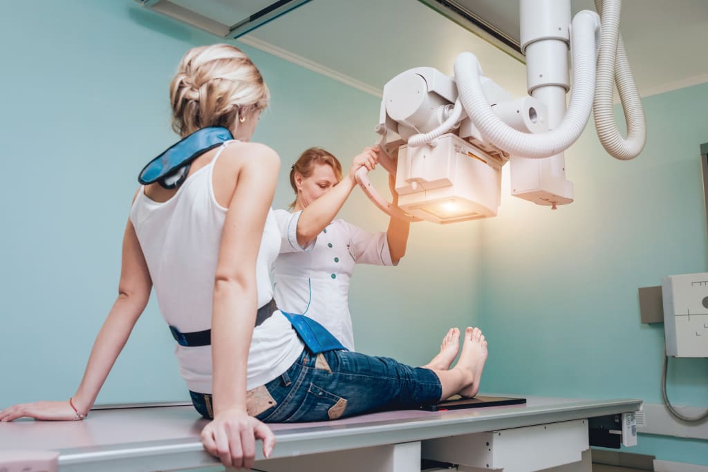 A female radiographer positioning the scanner while conducting a knee x-ray scan on a female patient.