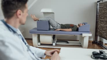 A male patient undergoes a DEXA scan, supervisied by a male doctor.