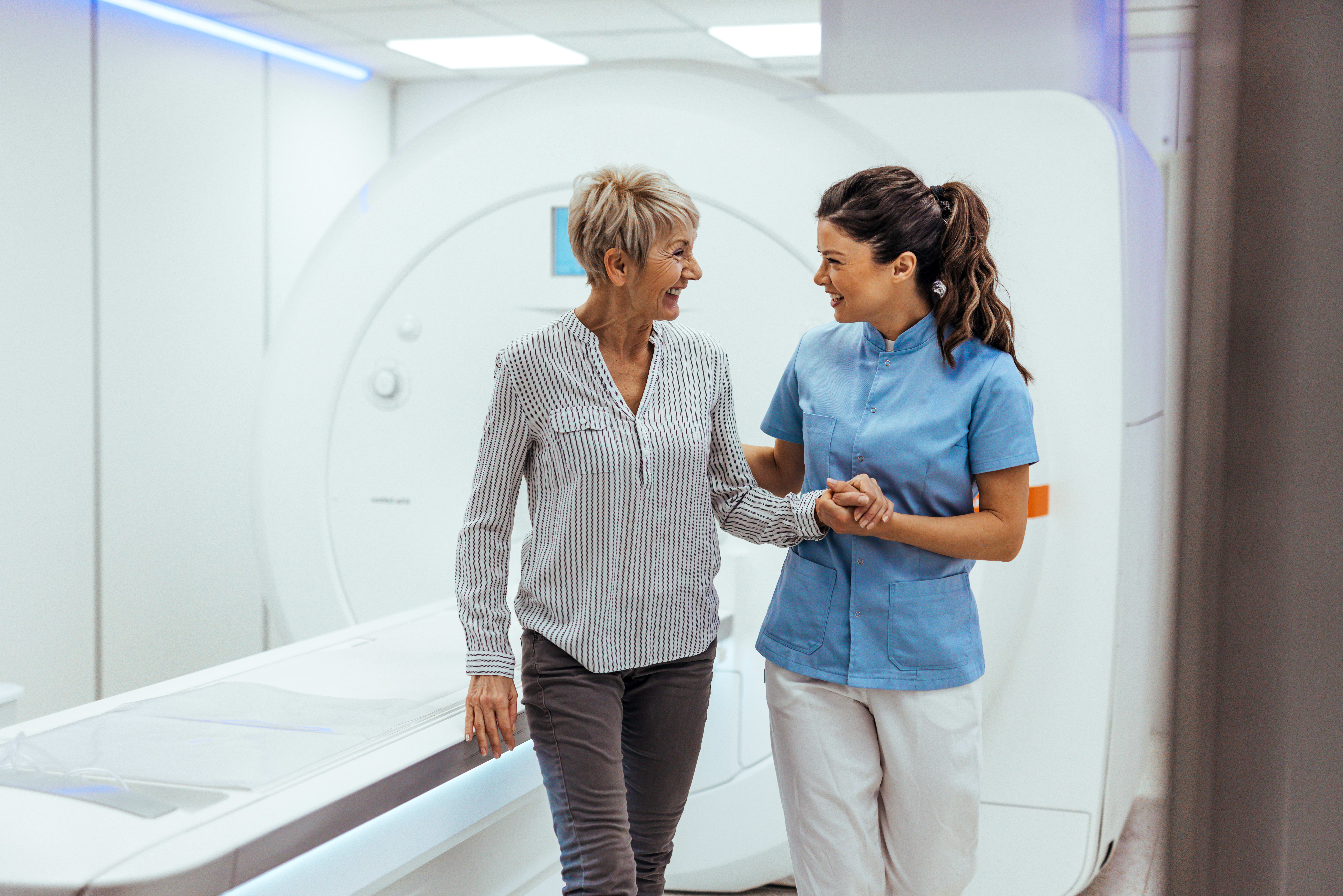A woman walks out from her MRI scan with a smiling radiology technician wearing scrubs.