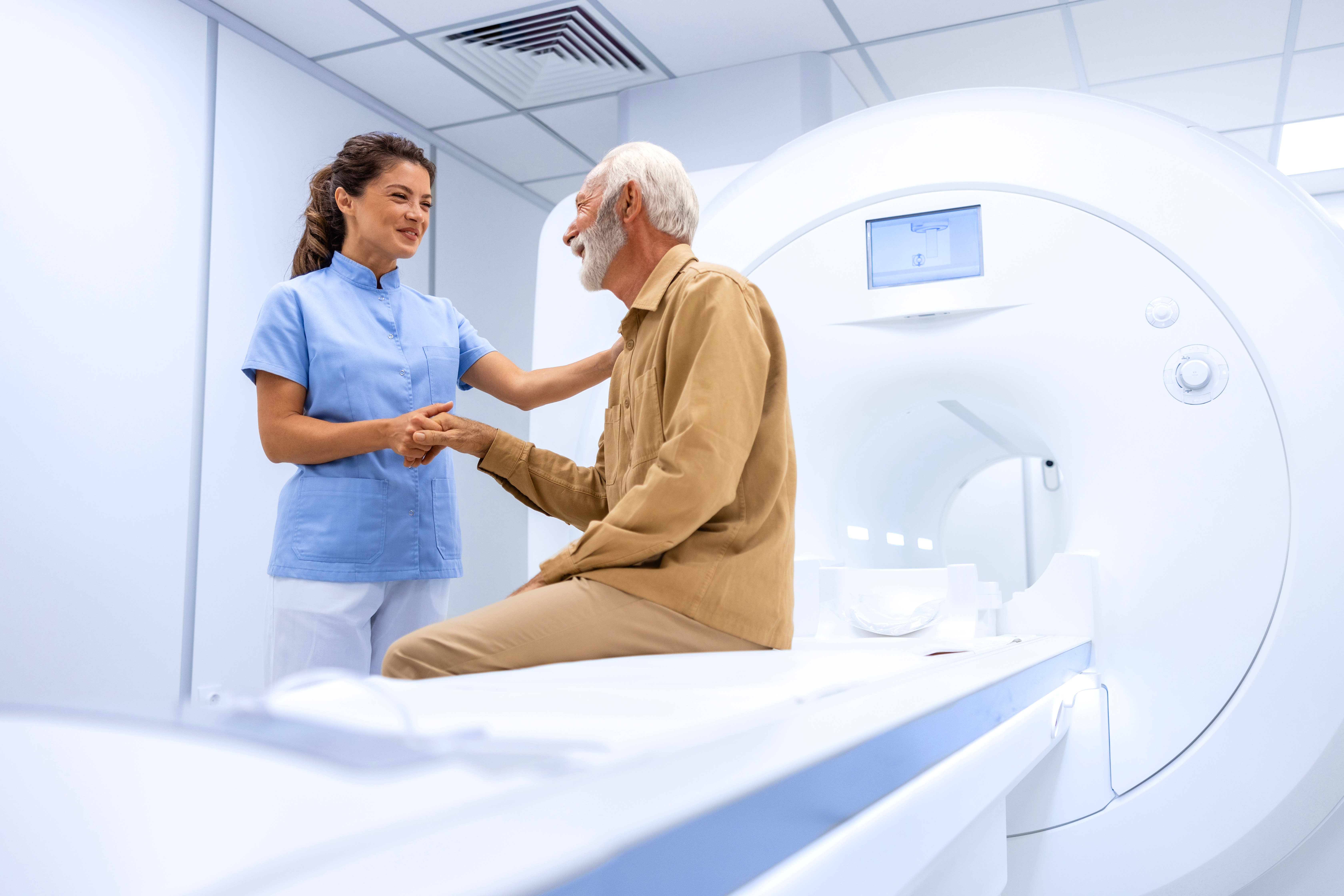 A man over 50 is speaking to a doctor before an MRI scan in a bright hospital MRI room.