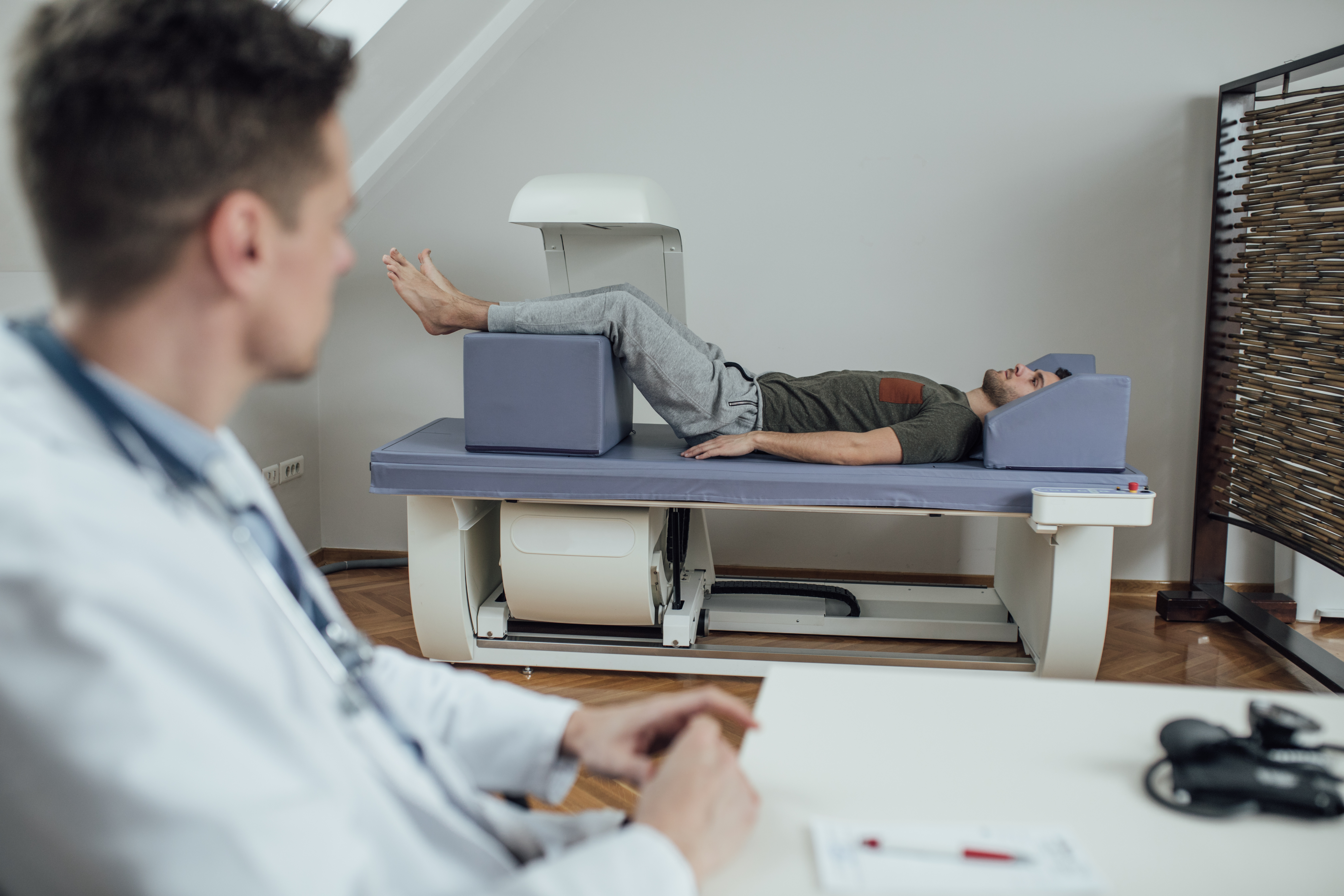 A male patient undergoes a DEXA scan, supervisied by a male doctor.
