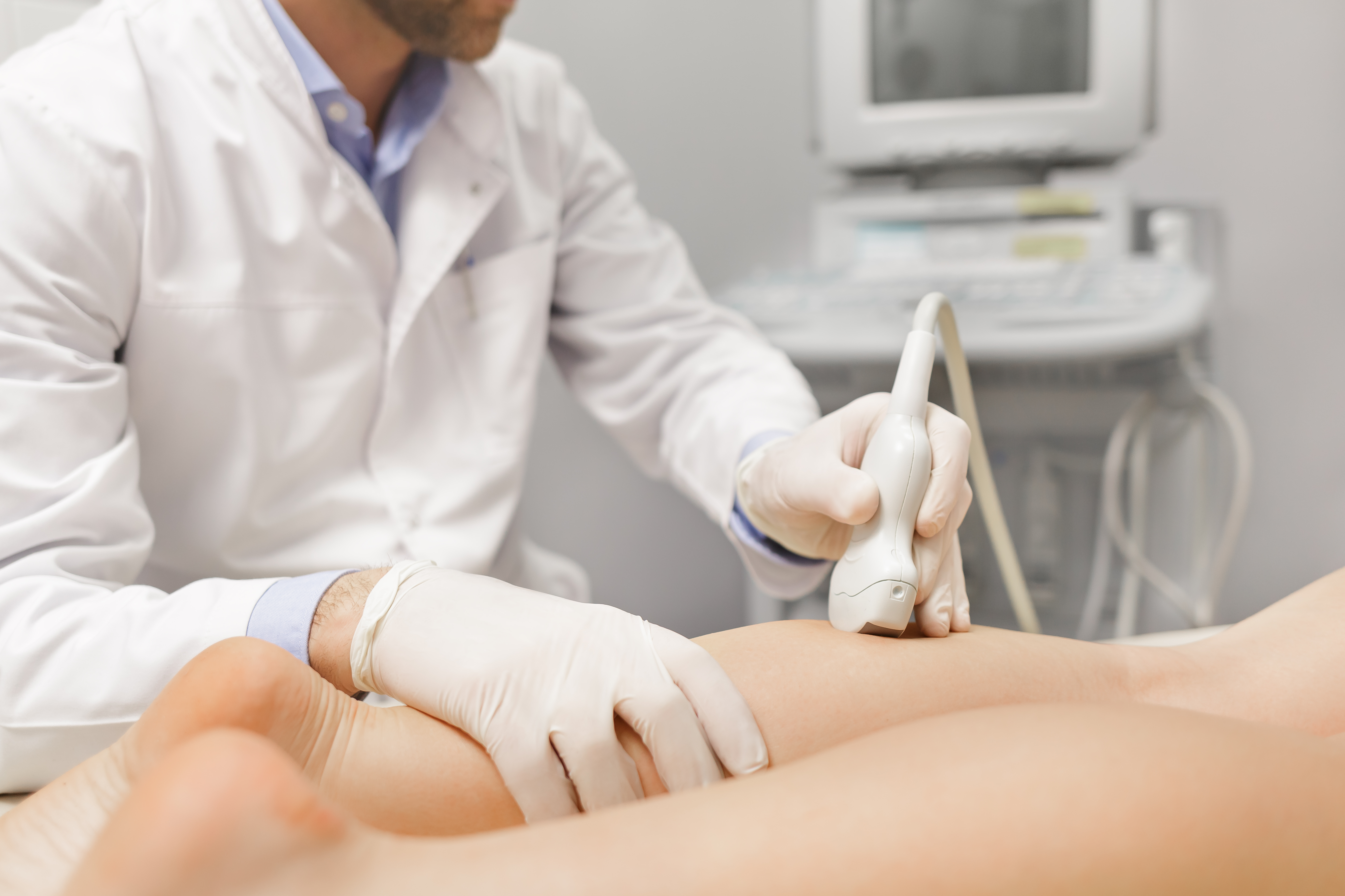 A medical professional wearing white gloves conducts an ultrasound scan of a person's calf muscle.