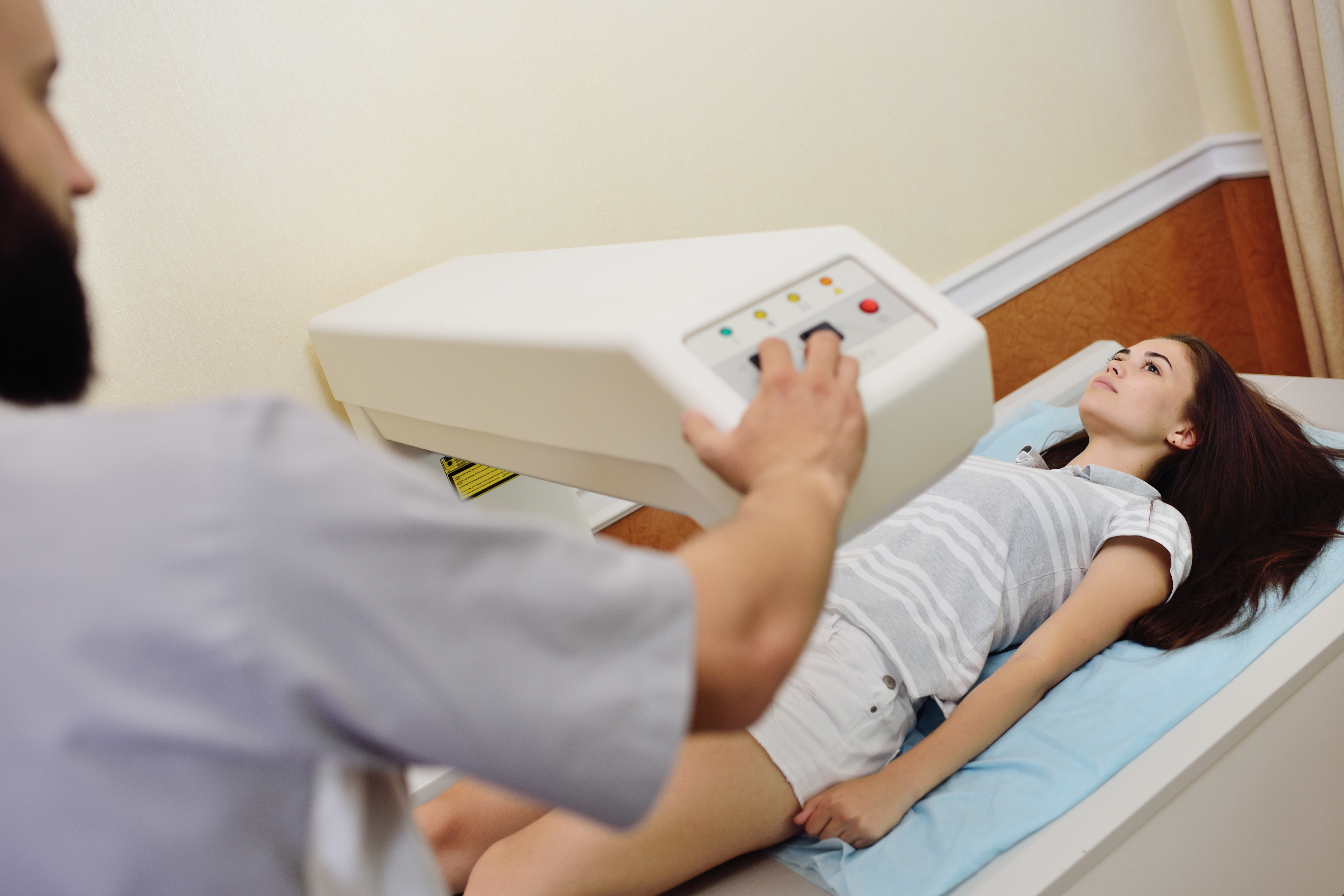 A male doctor conducts a DEXA scan on a young female patient.
