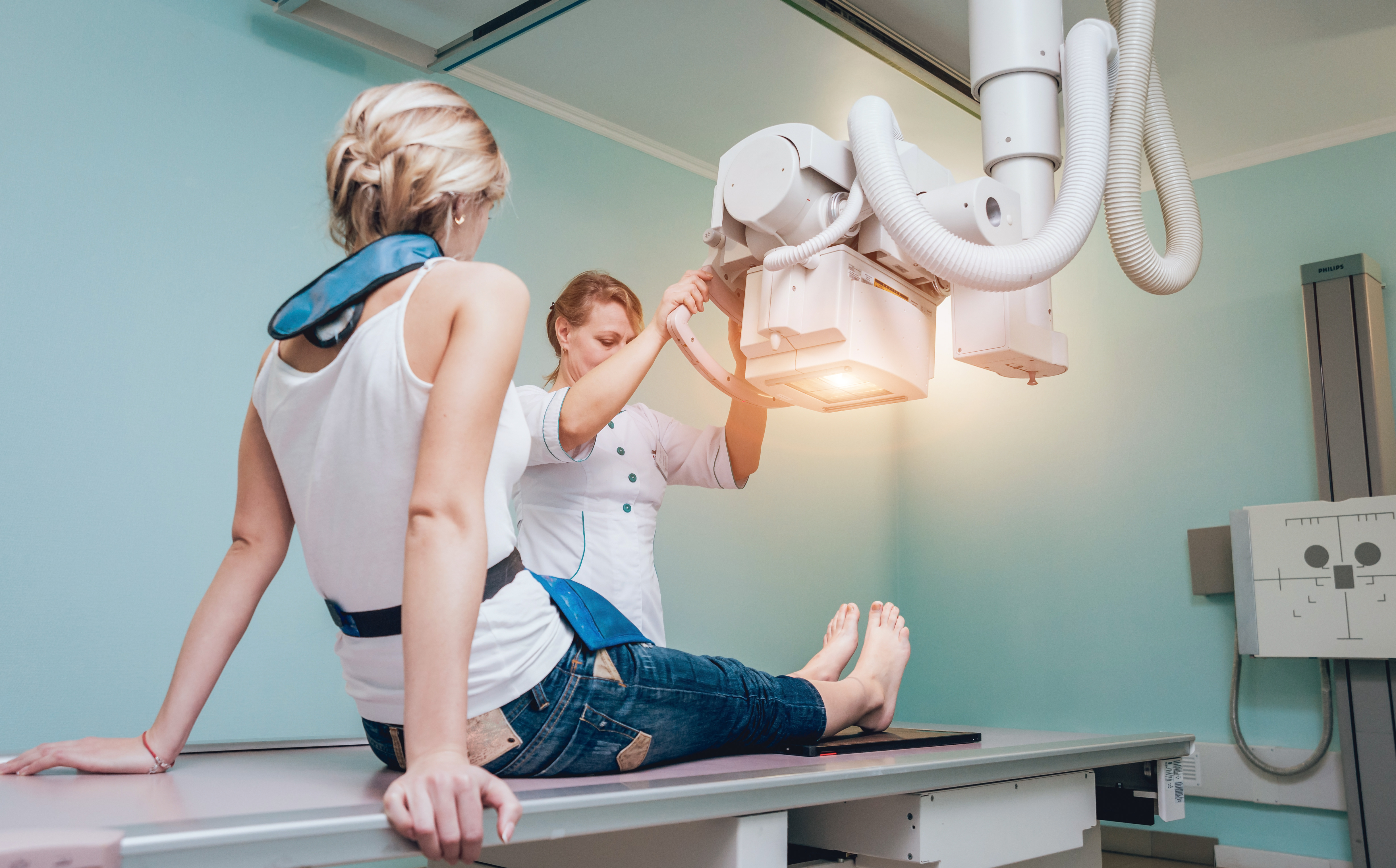 A female radiographer positioning the scanner while conducting a knee x-ray scan on a female patient.