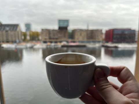 A hand holding a cup of espresso in front of a river view.