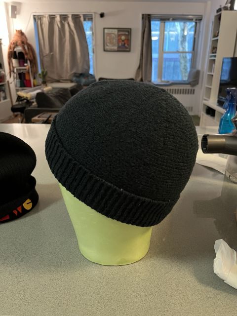 Black Chattie on pale green mannequin head, facing left.