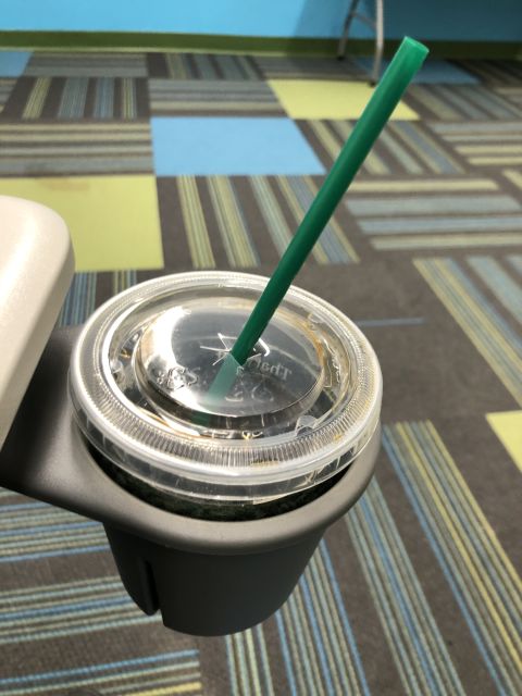 a plastic coffee cup with straw in a cupholder that hangs from a desk