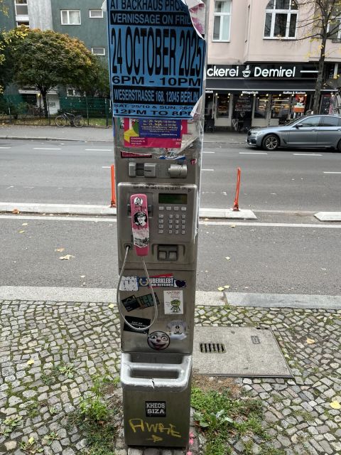 A pink-handset payphone on a pole, covered in stickers and flyers.