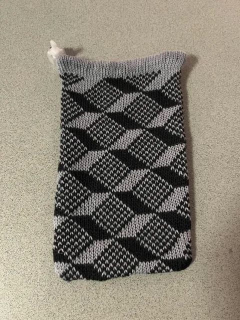 Empty bag laid flat on a countertop. At the top the gray hem and white 3D printed lace lock are visible, then the cube-patterned body in gray and black, ending in at the bottom with slightly rounded edges.