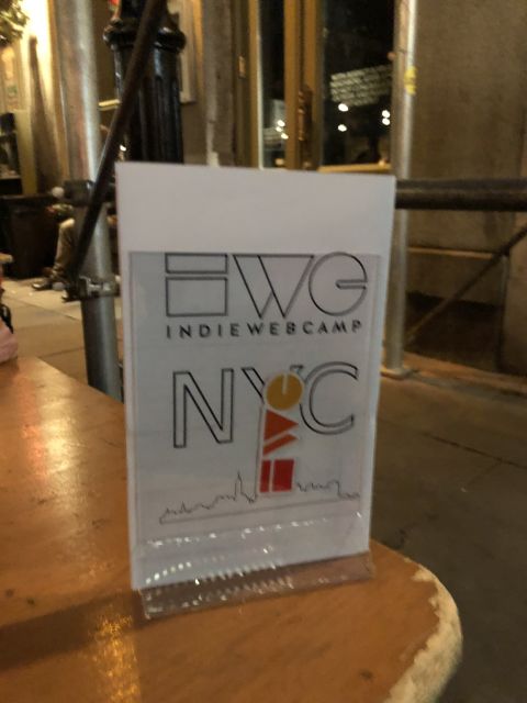 a document stand on a wooden table holds a sign announcing IWC NYC