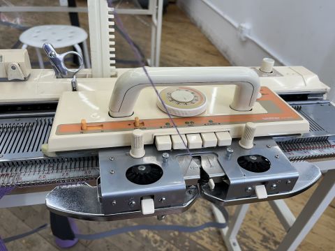 Brother KH-860 knitting machine carriage resting at the right edge of the needle bed. Purple yarn is in the A feeder slot.
