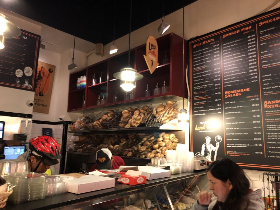 a glass-front deli counter filled with spreads in front of a wall of bagels