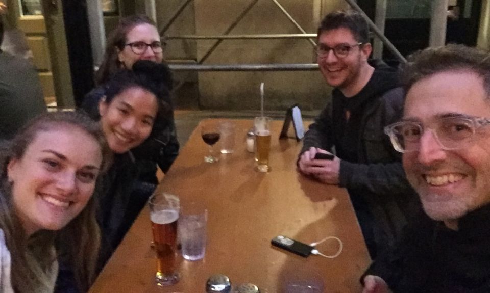 5 smiling people sitting around a table outside at dusk