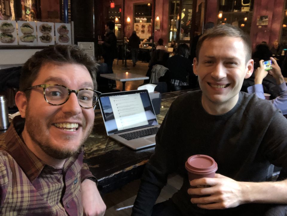 Marty and Dmitri smile at the camera. Behind them coffee shop patrons go about their business.