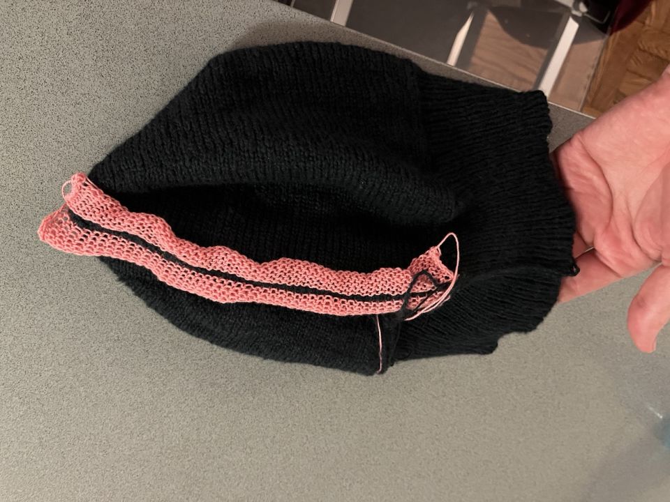 Showing off the grafted side seam, with pink waste yarn still visible. A hand is lifting up the ribbed brim to get better light on the visible seam there.